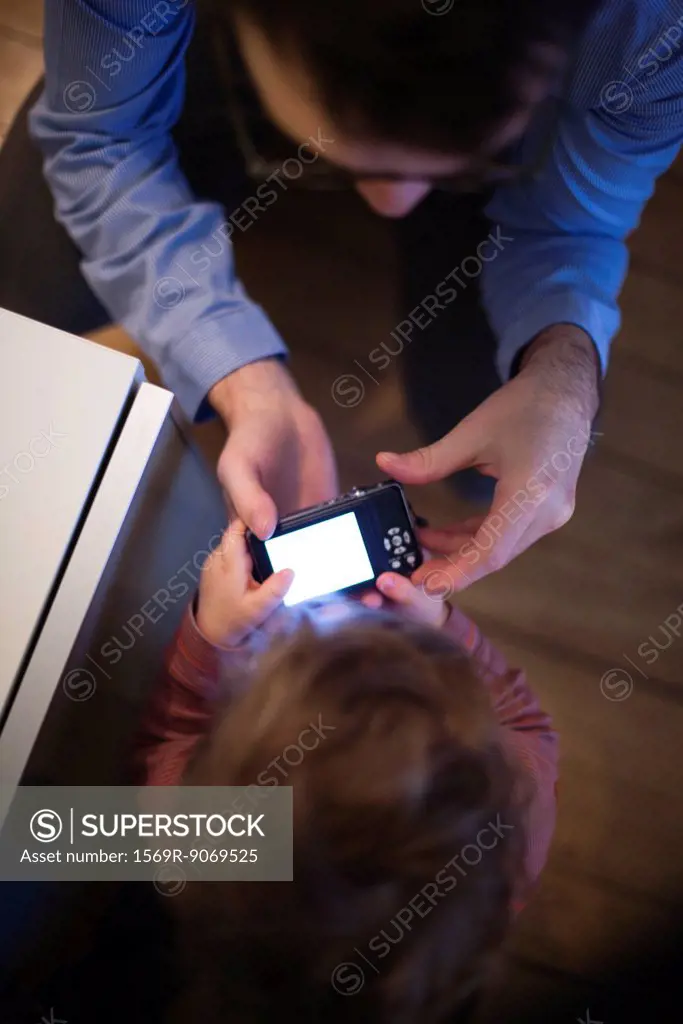 Father and young son looking at digital camera together, overhead view