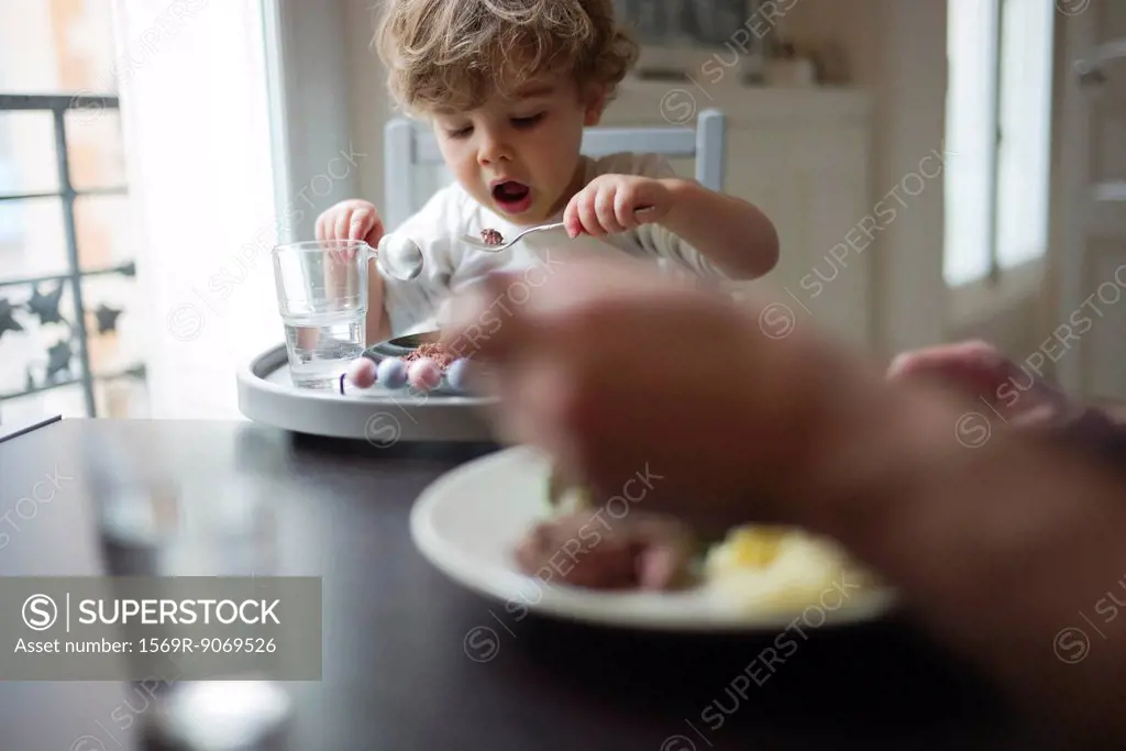 Toddler boy eating meal with parent