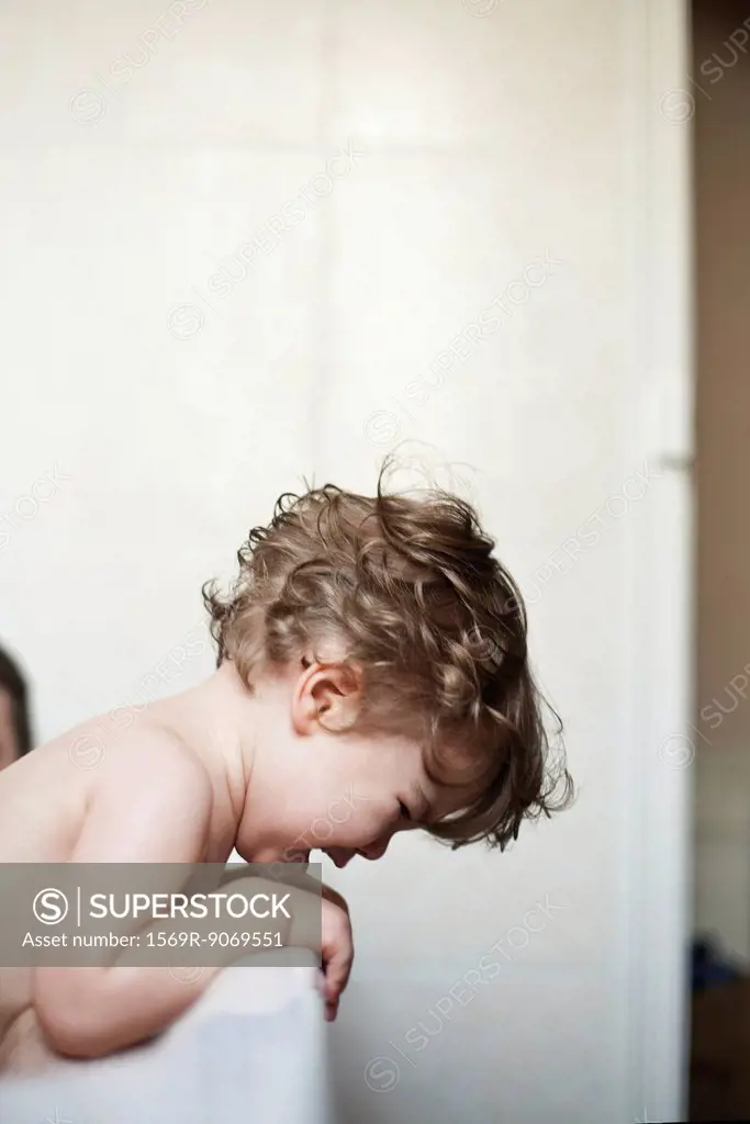 Toddler boy leaning over side of bathtub crying