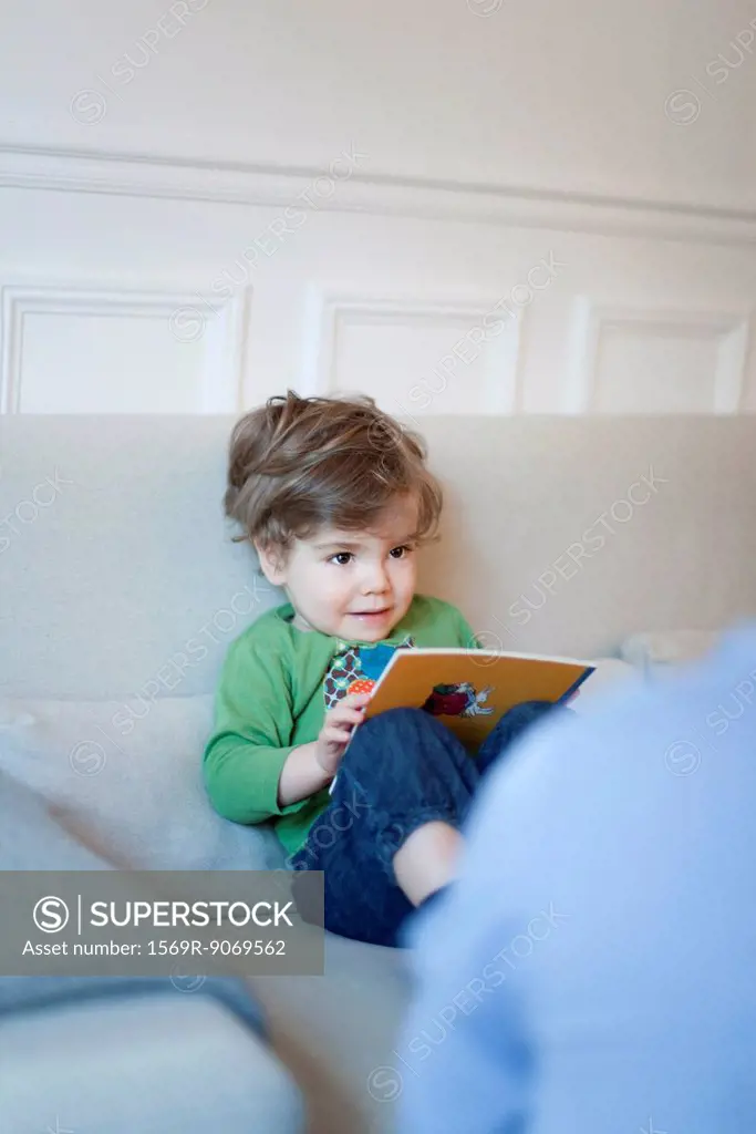 Toddler boy sitting on couch with book in hands