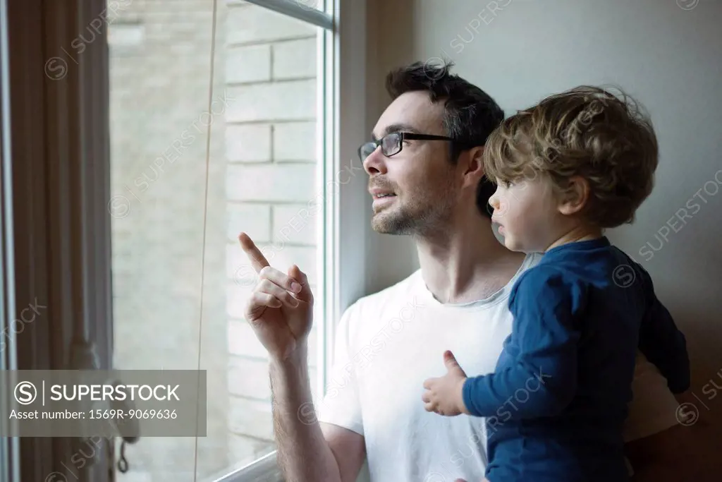Father and toddler son looking out window together