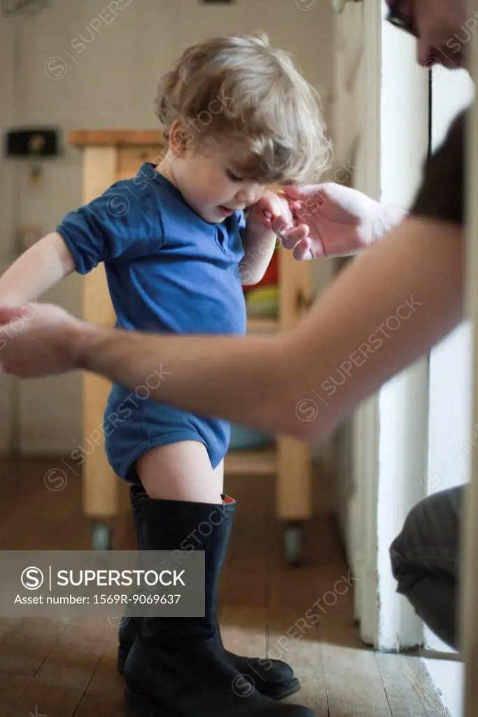 Toddler boy learning to walk in father´s boots