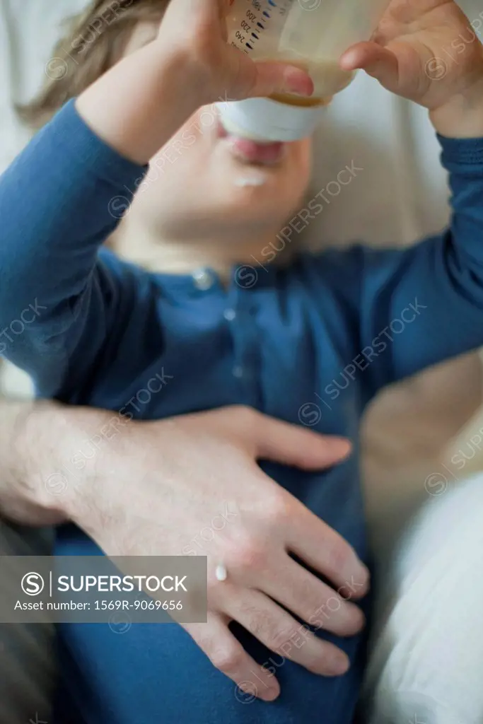 Toddler boy drinking milk from bottle in father´s arms