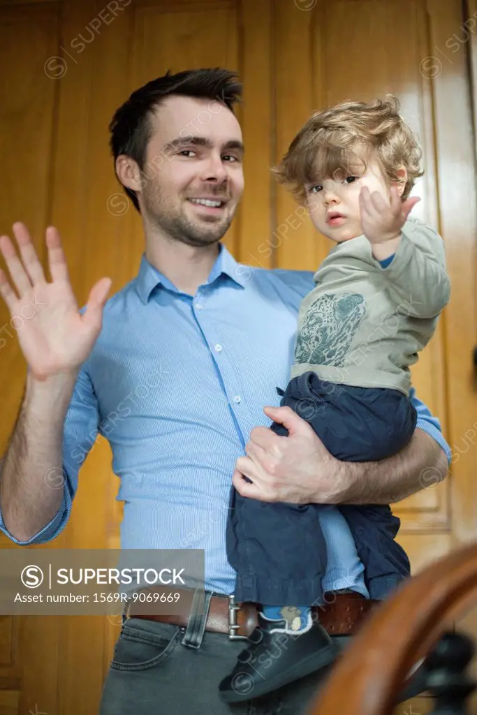 Father and toddler son waving at camera