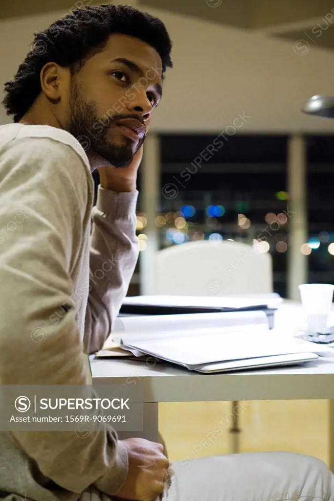 Man sitting at desk in office at night, looking away in thought