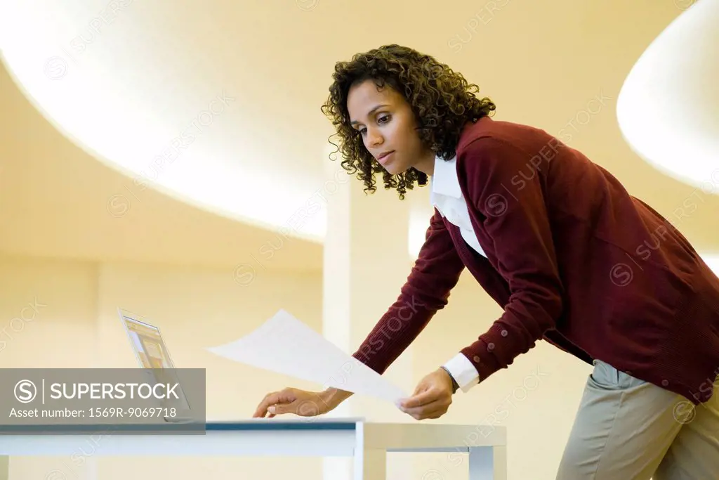 Businesswoman using laptop computer and looking at document