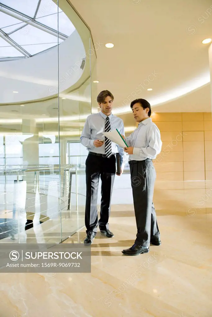 Businessmen discussing document in corridor