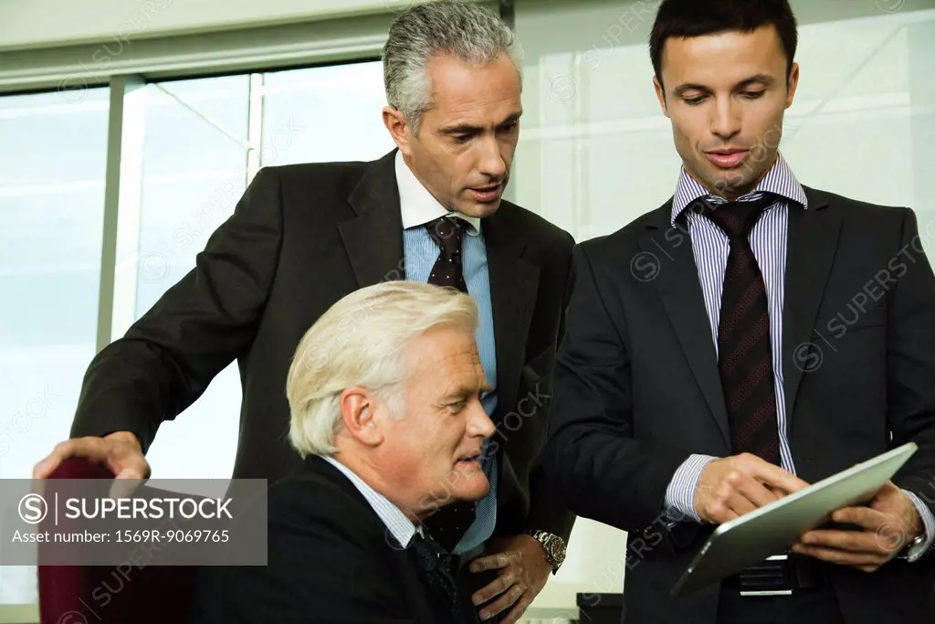 Young businessman showing mature executives how to use digital tablet