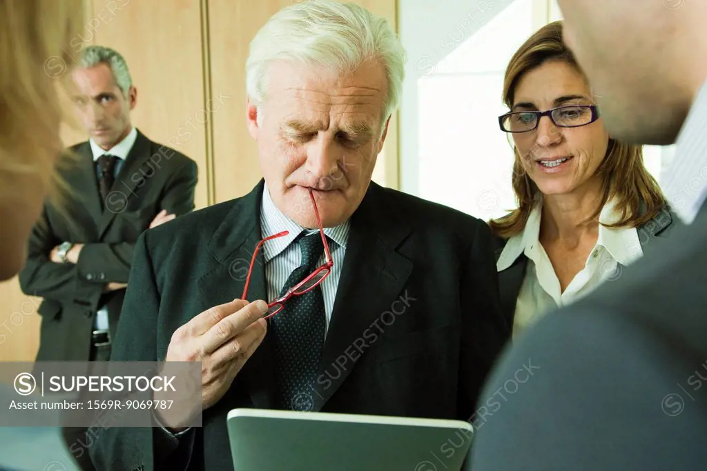 Mature executive examining information on digital tablet with colleagues