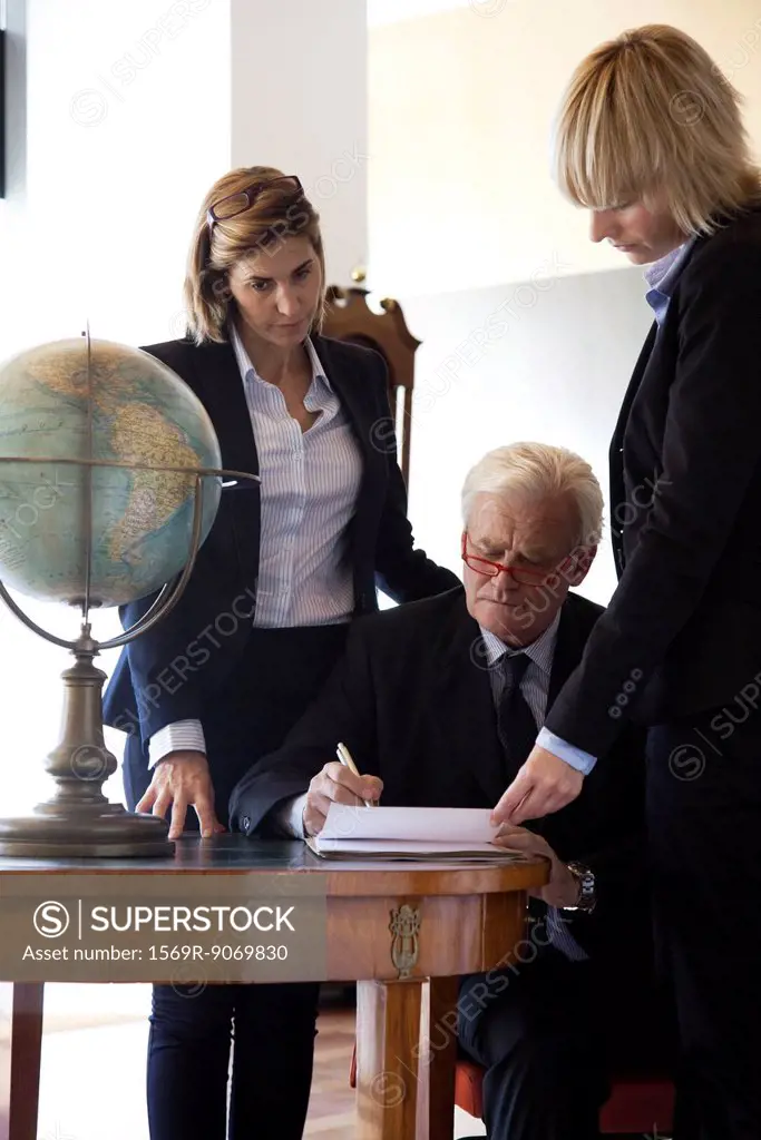 Executive signing paperwork, colleagues by his side