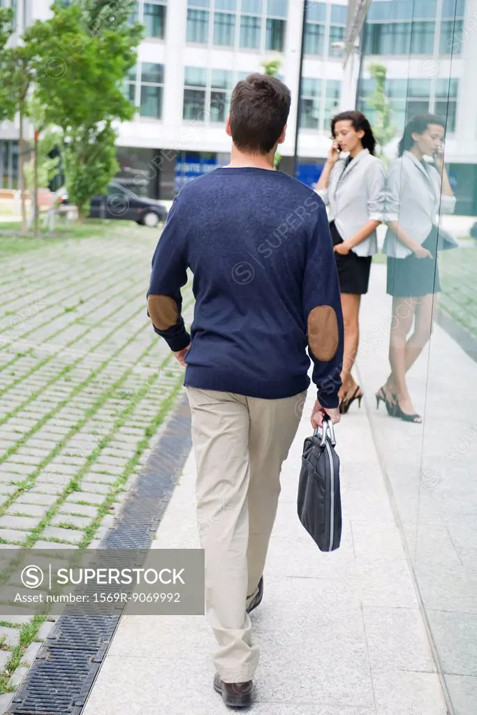 Man walking with briefcase, woman talking on cell phone in background
