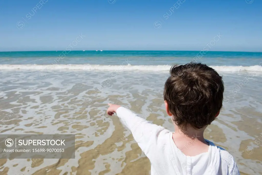 Little boy at the beach, pointing at sea, rear view