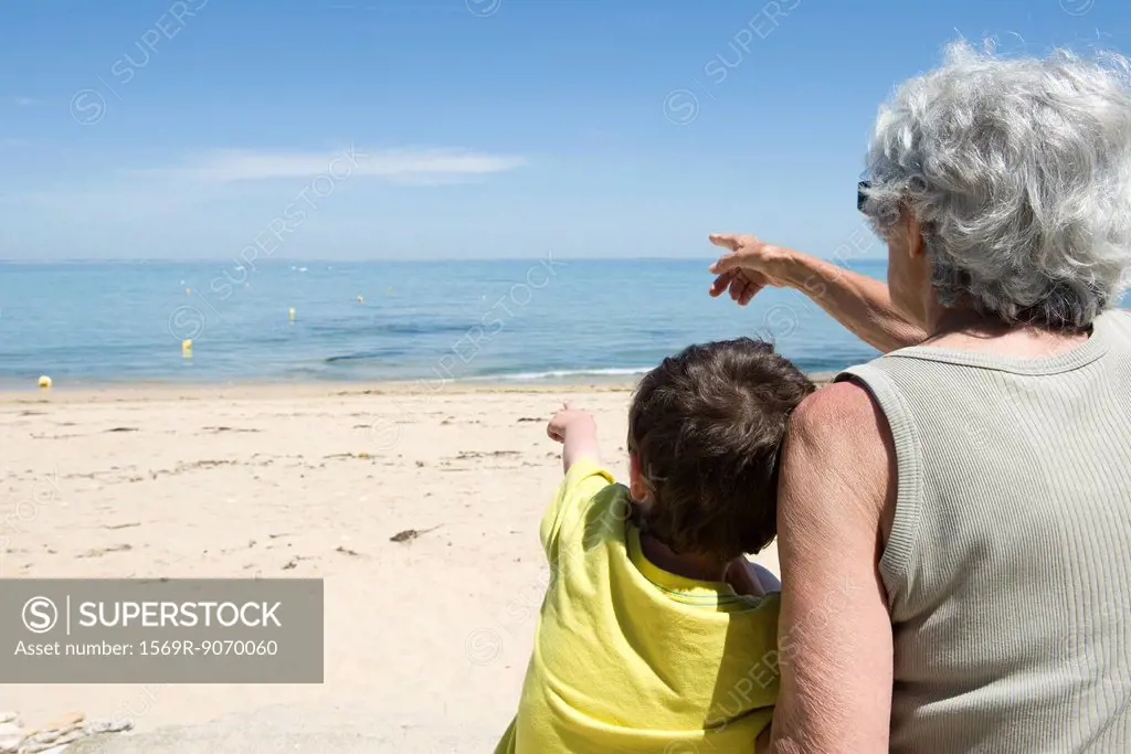 Grandmother and grandson sitting together on beach, looking at sea