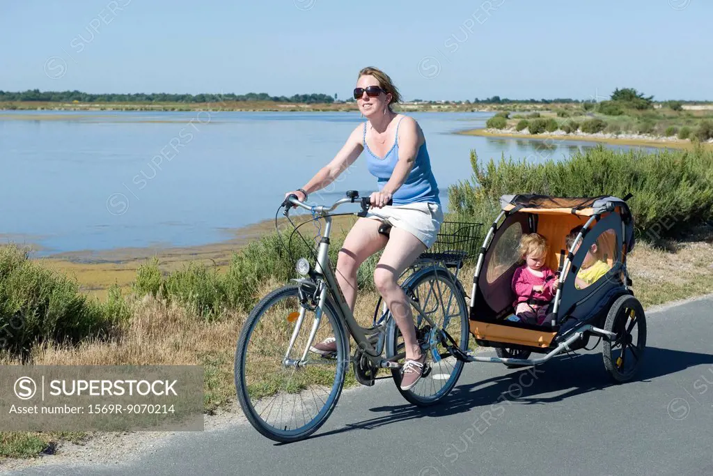 Woman riding along bicycle path with children in bicycle trailer
