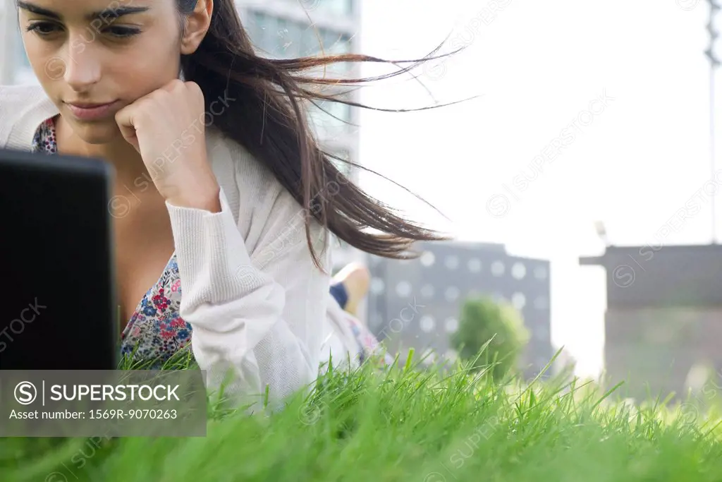 Young woman lying on stomach on grass with hair blowing in wind