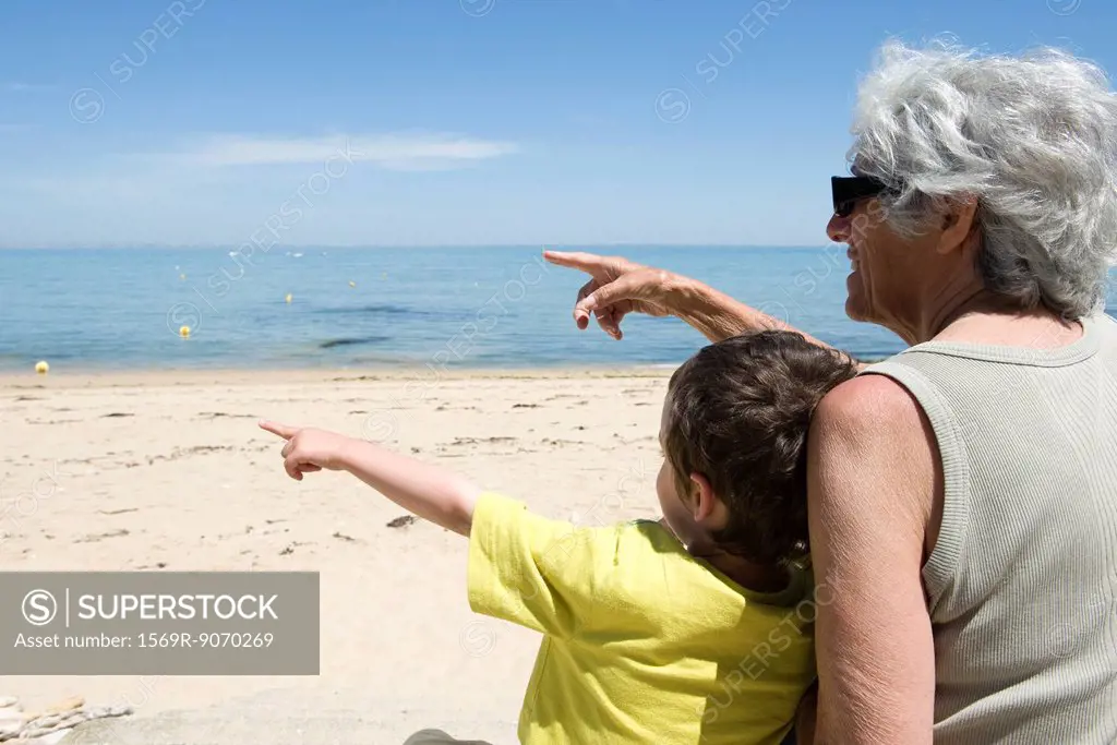 Grandmother and grandson sitting together on beach, pointing at sea
