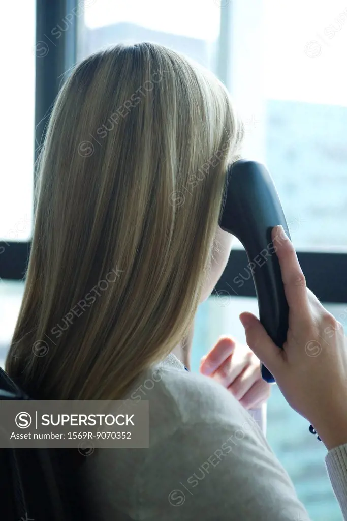 Woman looking out window while talking on landline phone, rear view