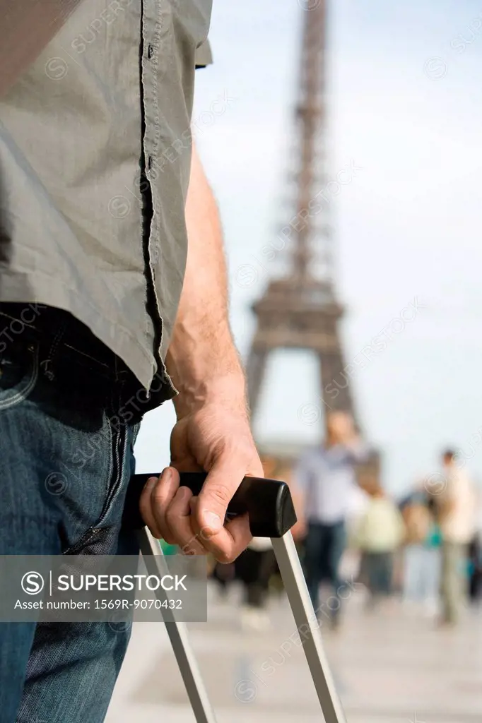 Man holding handle of rolling suitcase, Eiffel Tower visible in background, Paris, France