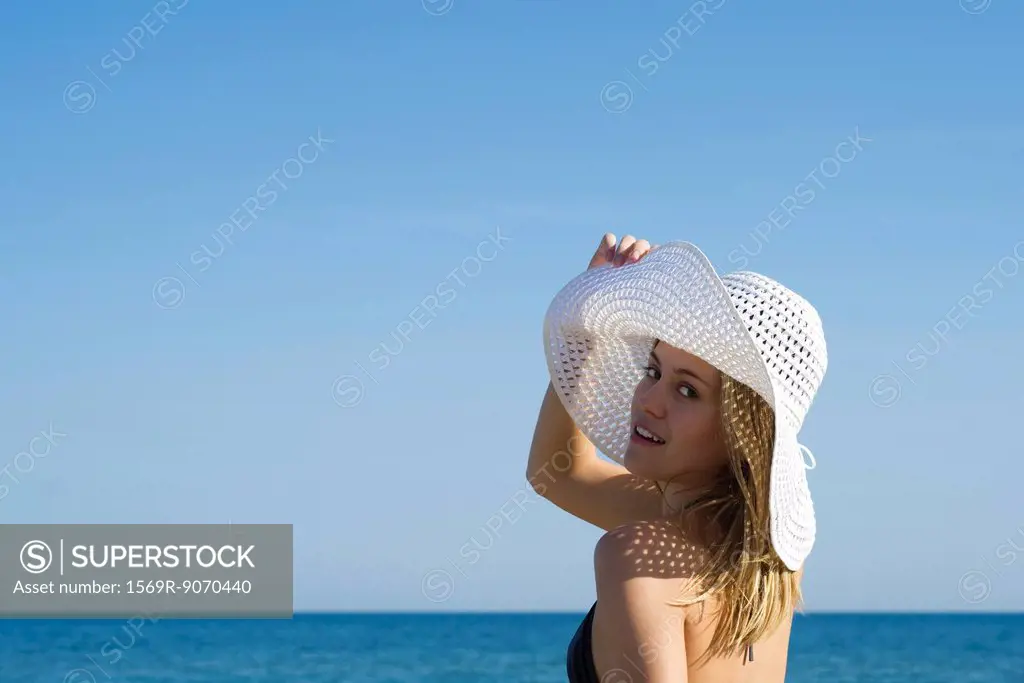 Woman wearing sun hat at the beach, looking over shoulder, portrait