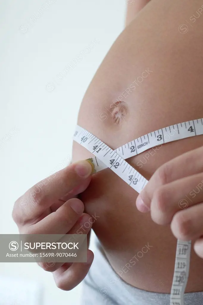 Pregnant woman measuring her belly with measuring tape, cropped