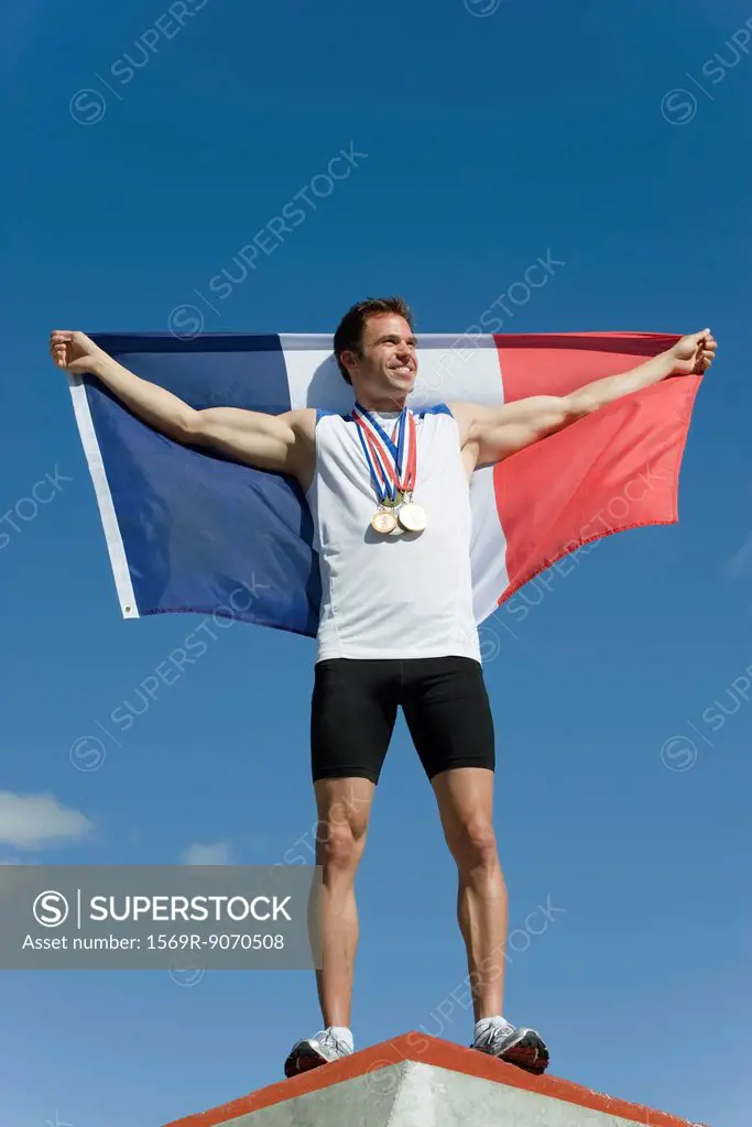 Male athlete being honored on podium, holding up French flag