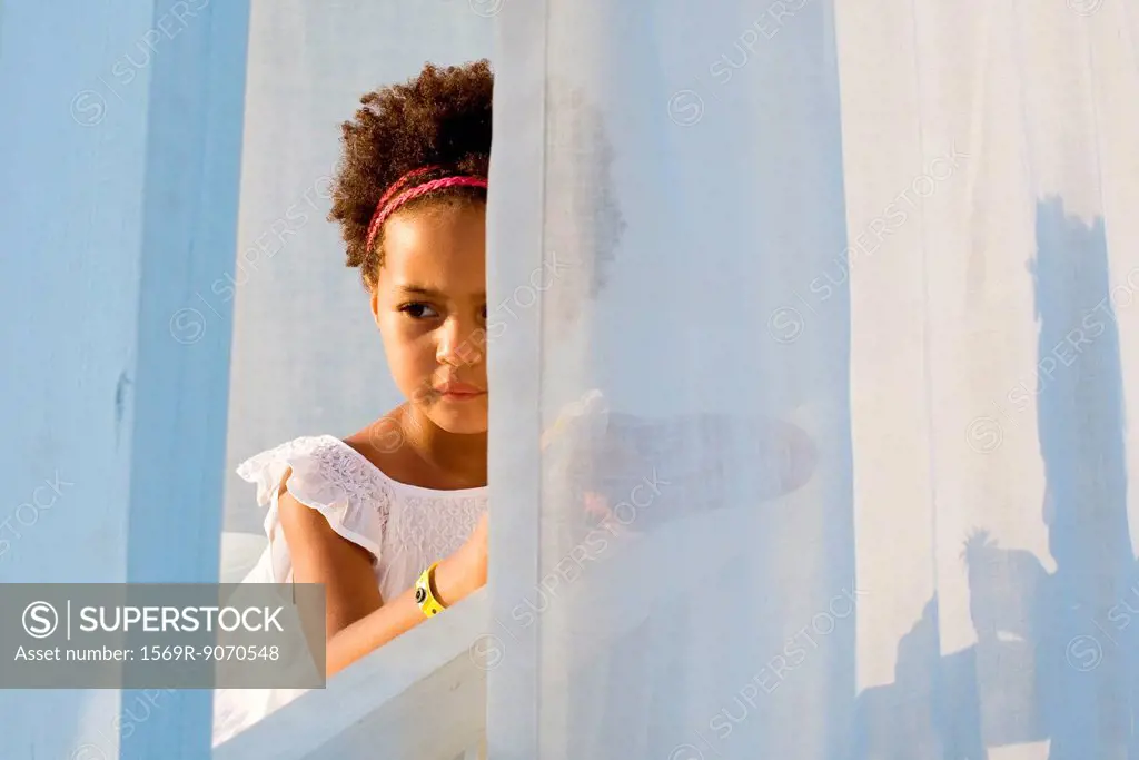 Little girl looking through curtain, portrait