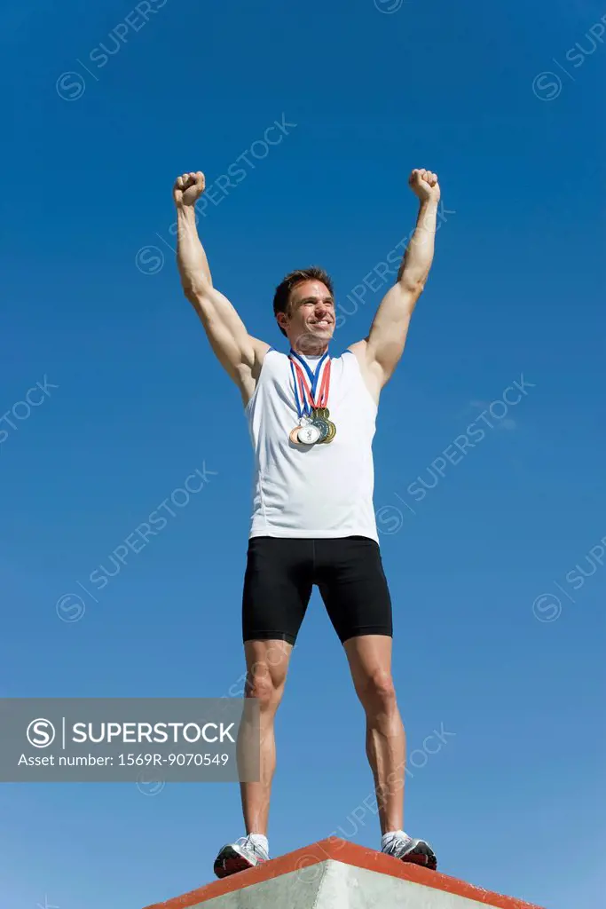 Male athlete standing on winner´s podium with arms raised in victory