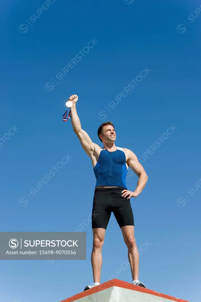 Male athlete on podium, holding up gold medal