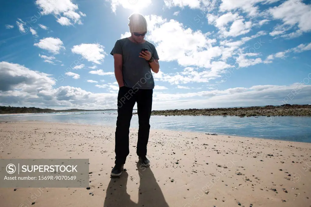 Man standing on beach, looking at cell phone