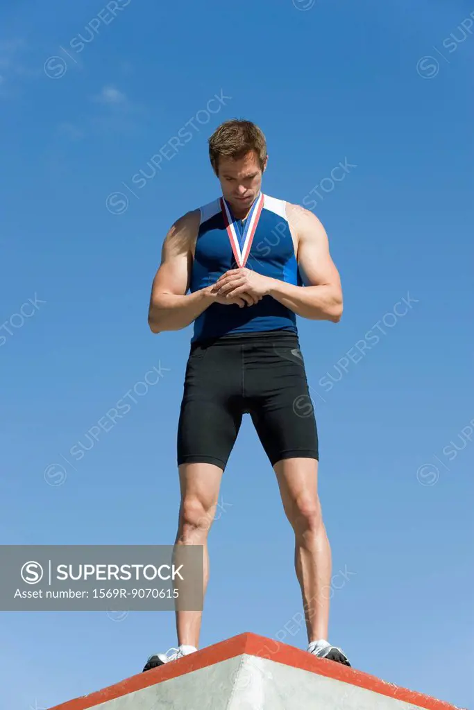 Male athlete on winner´s podium, holding medal and looking down