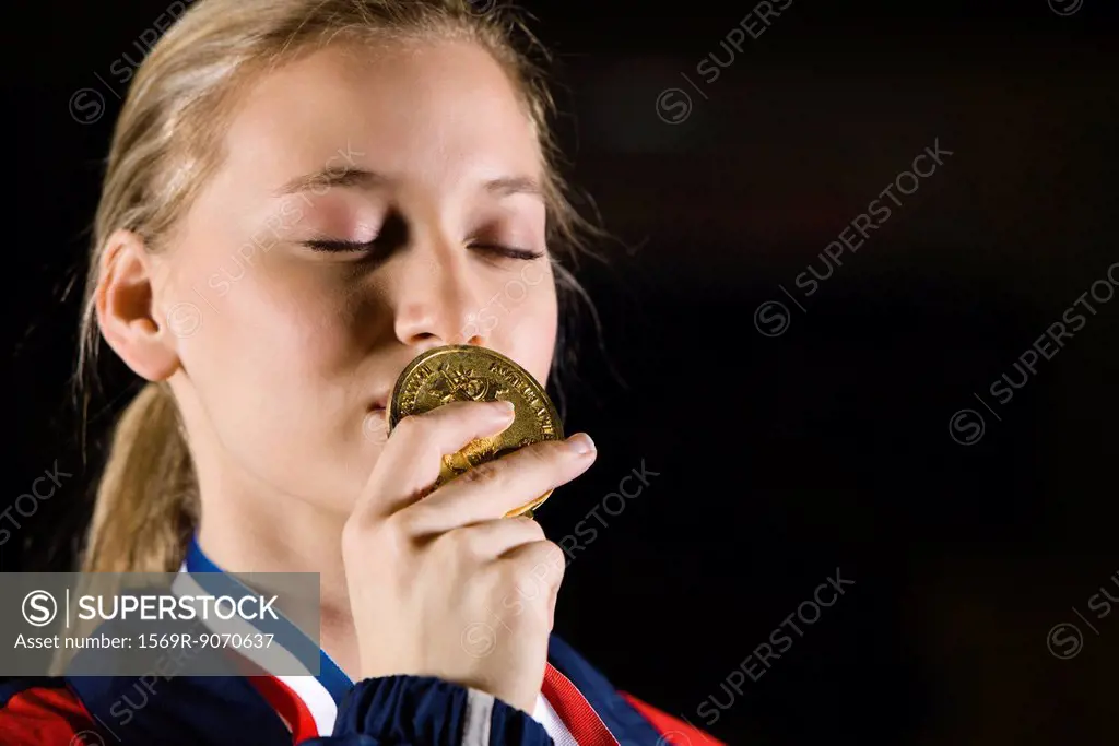 Female athlete kissing gold medal, portrait