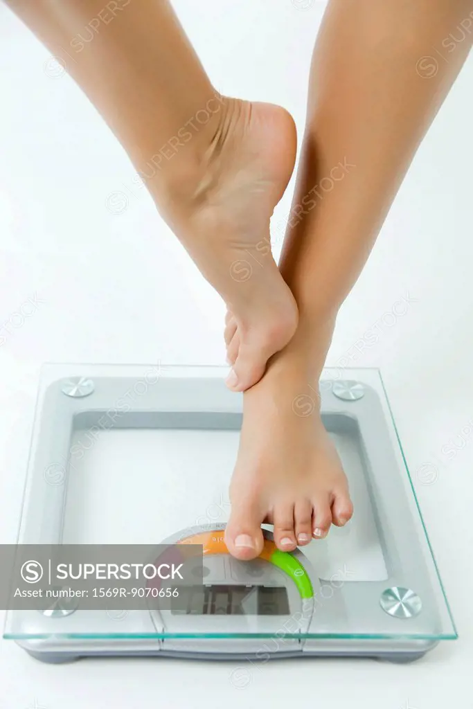 Woman standing on one leg on bathroom scale, low section