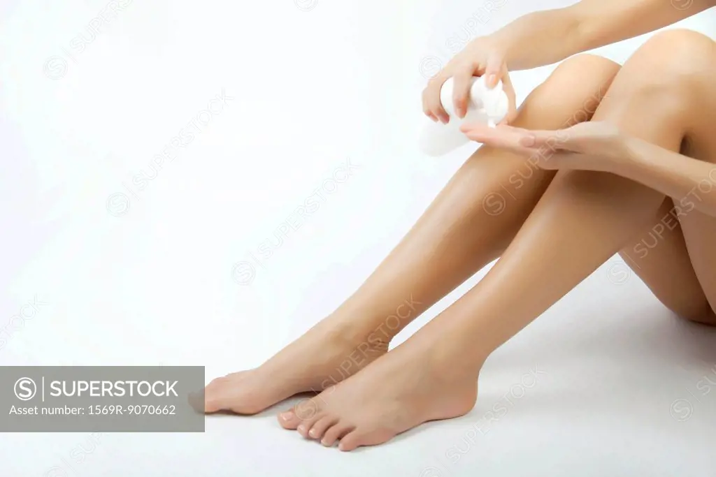 Woman moisturizing legs, cropped
