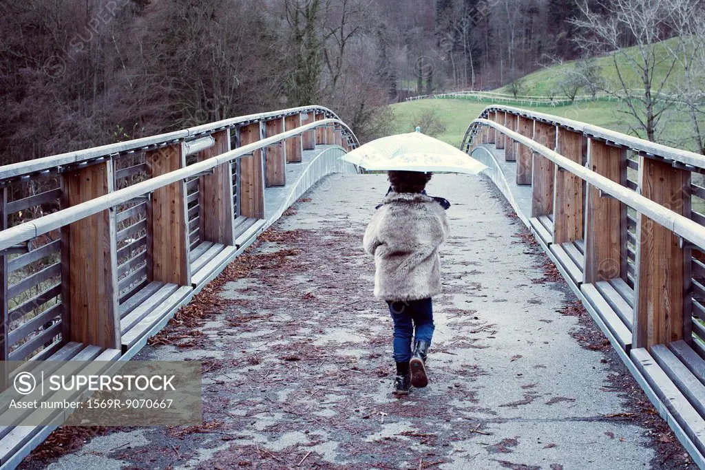 Girl walking on bridge with umbrella, rear view