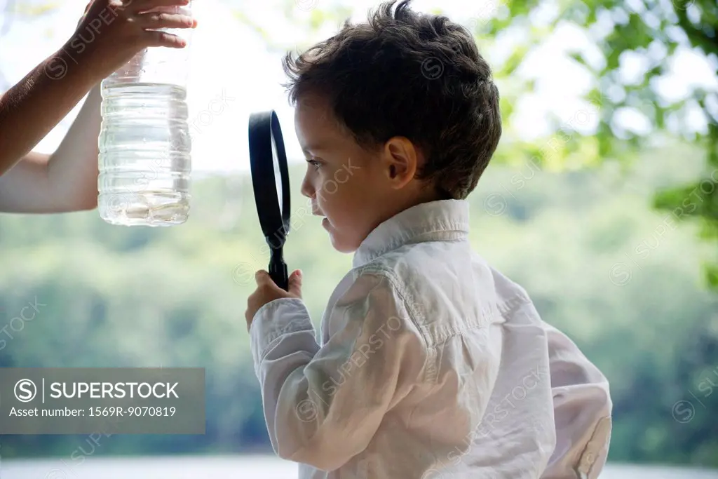 Boy studying fish in water bottle with magnifying glass