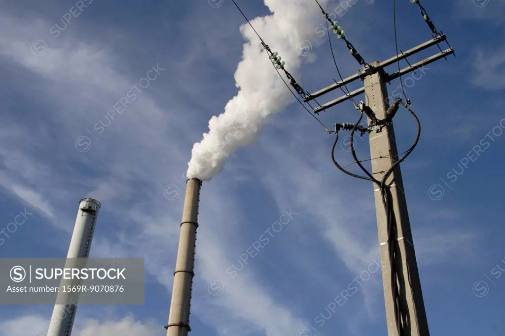 Electric post and smokestack against sky