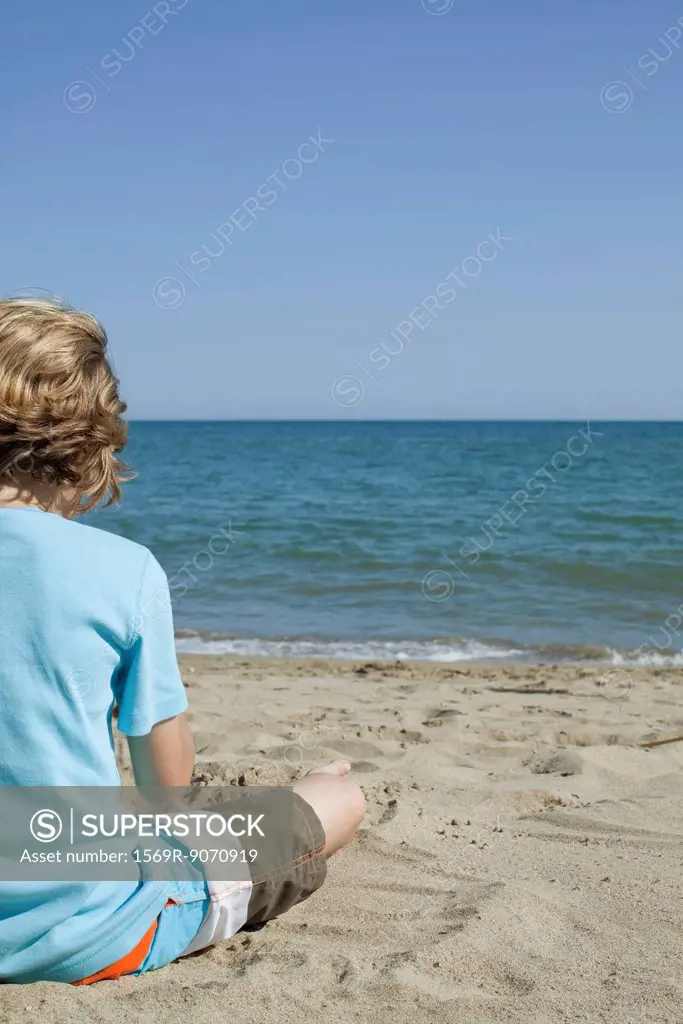 Boy sitting on beach, looking at sea