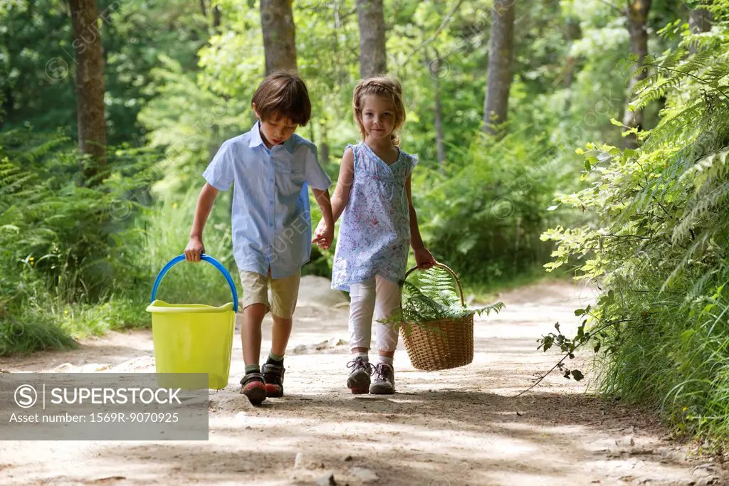 Children walking hand in hand in woods, carrying basket and bucket