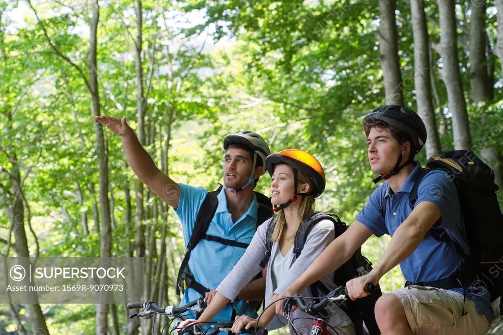 Friends bike riding in woods, man gesturing into distance