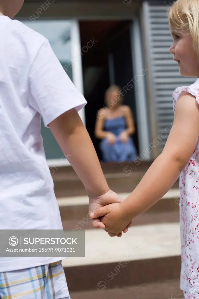 Young siblings holding hands outdoors, rear view