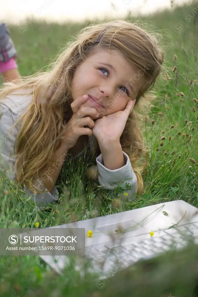 Girl lying in grass with laptop computer, daydreaming