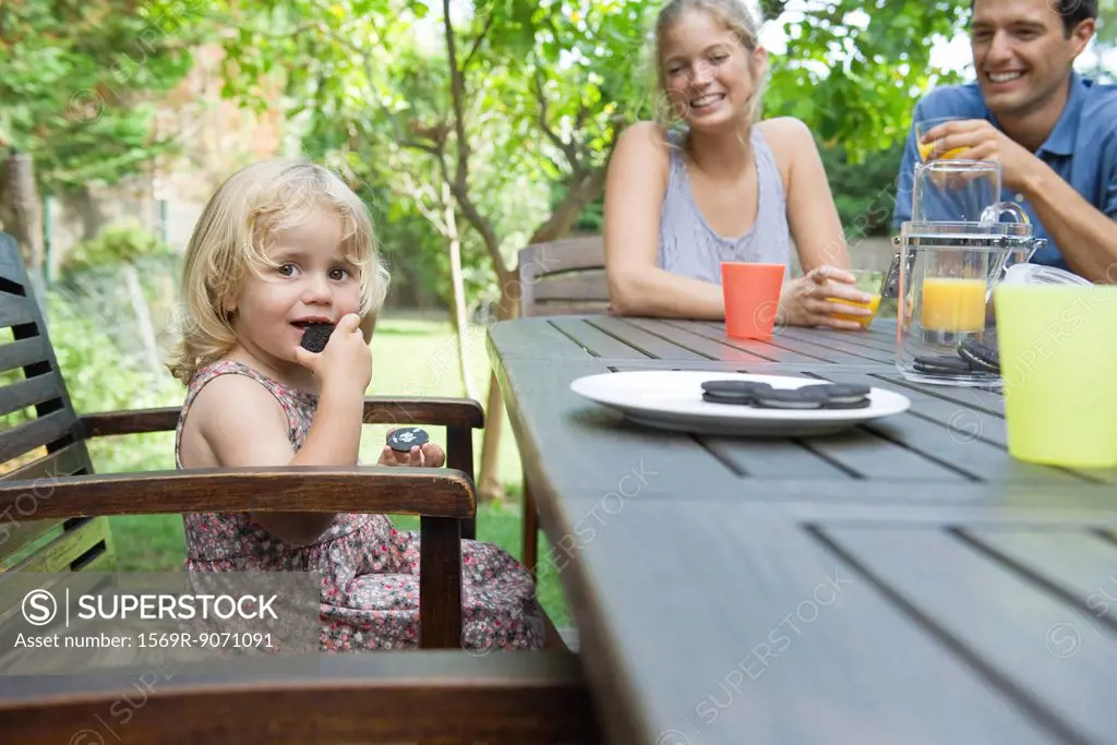 Little girl eating snack with her parents outdoors