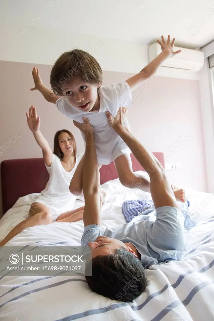 Family together on bed, father lifting son in the air