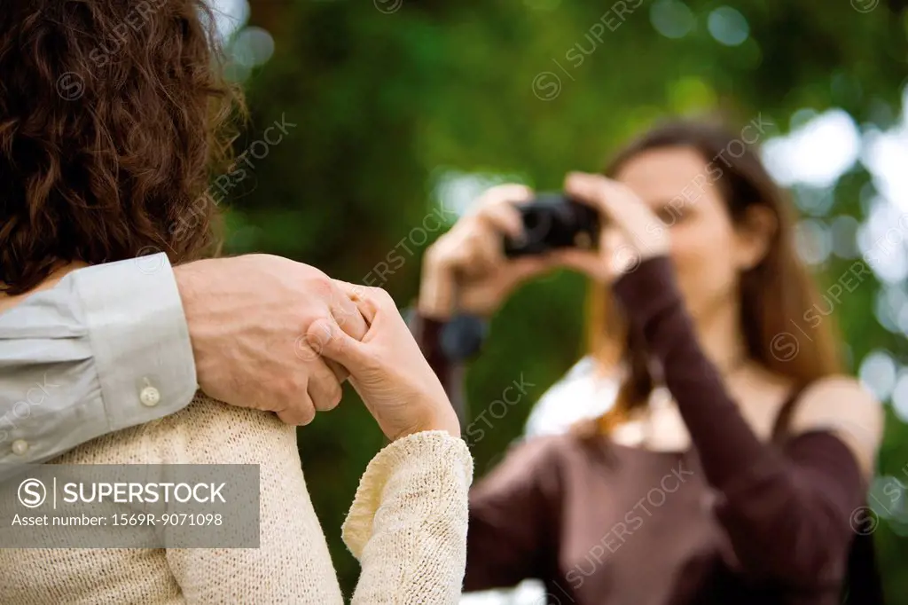 Couple holding hands as woman photographs them, cropped