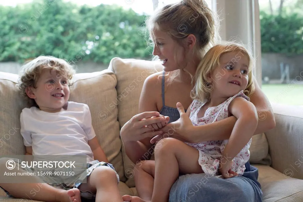 Mother and two young children sitting together on sofa