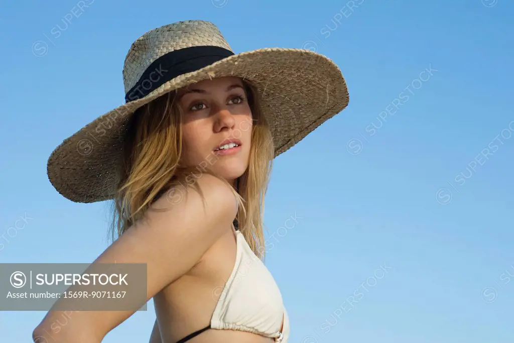 Woman in bikini and sunhat looking away in thought, portrait