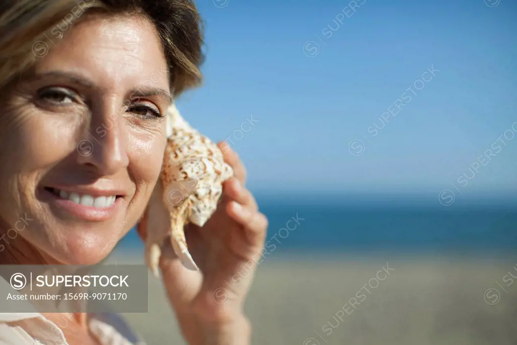 Woman listening to seashell, portrait