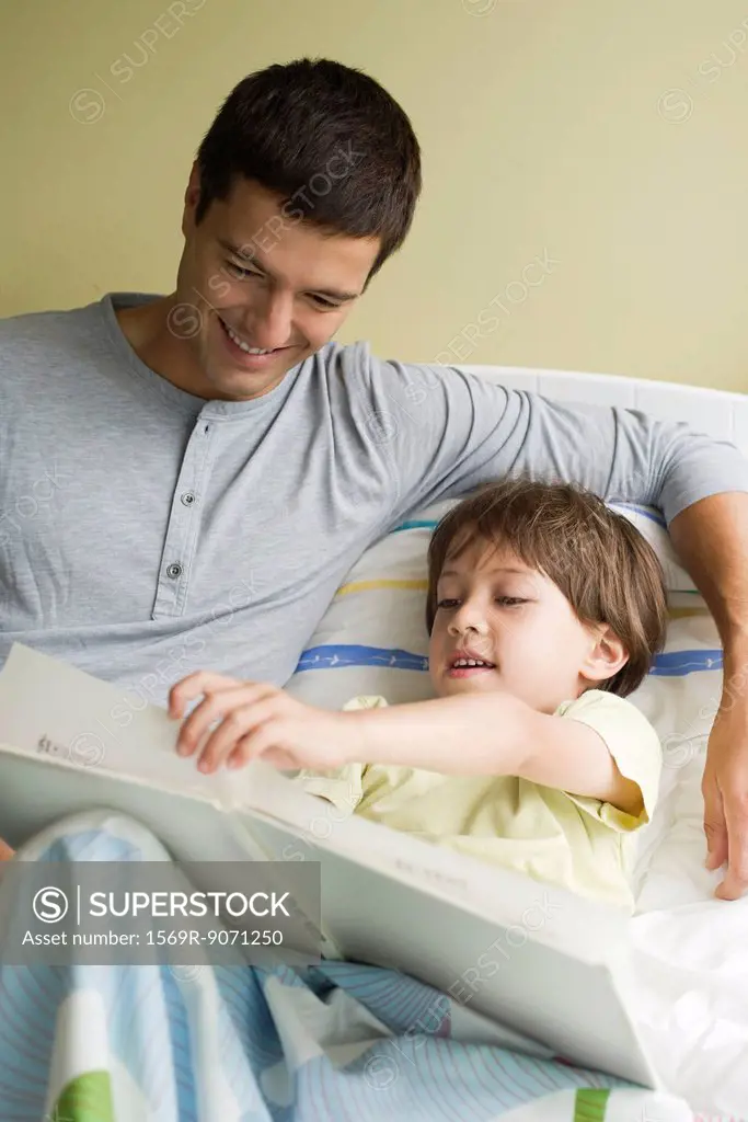 Father and son reading book together in bed