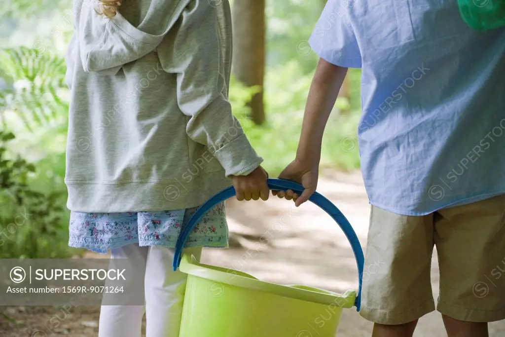 Children carrying bucket together, cropped