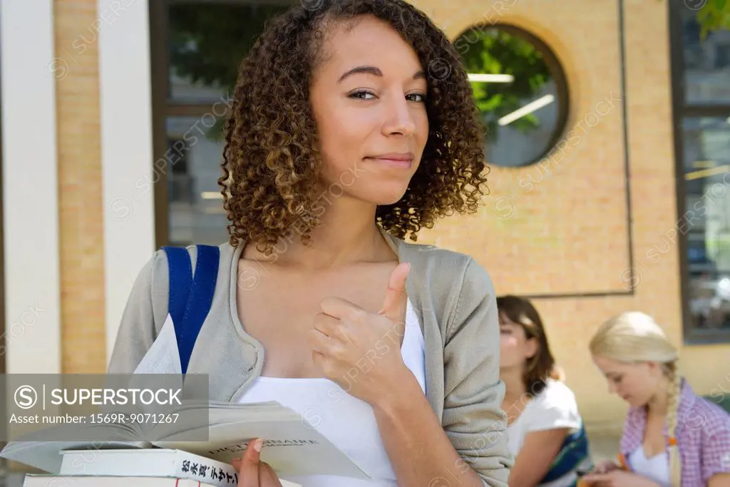 Female college student giving thumbs up sign, portrait